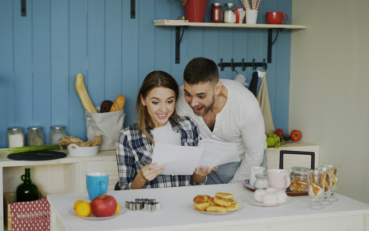 Sepasang suami istri melihat berkas bersama di meja dapur
